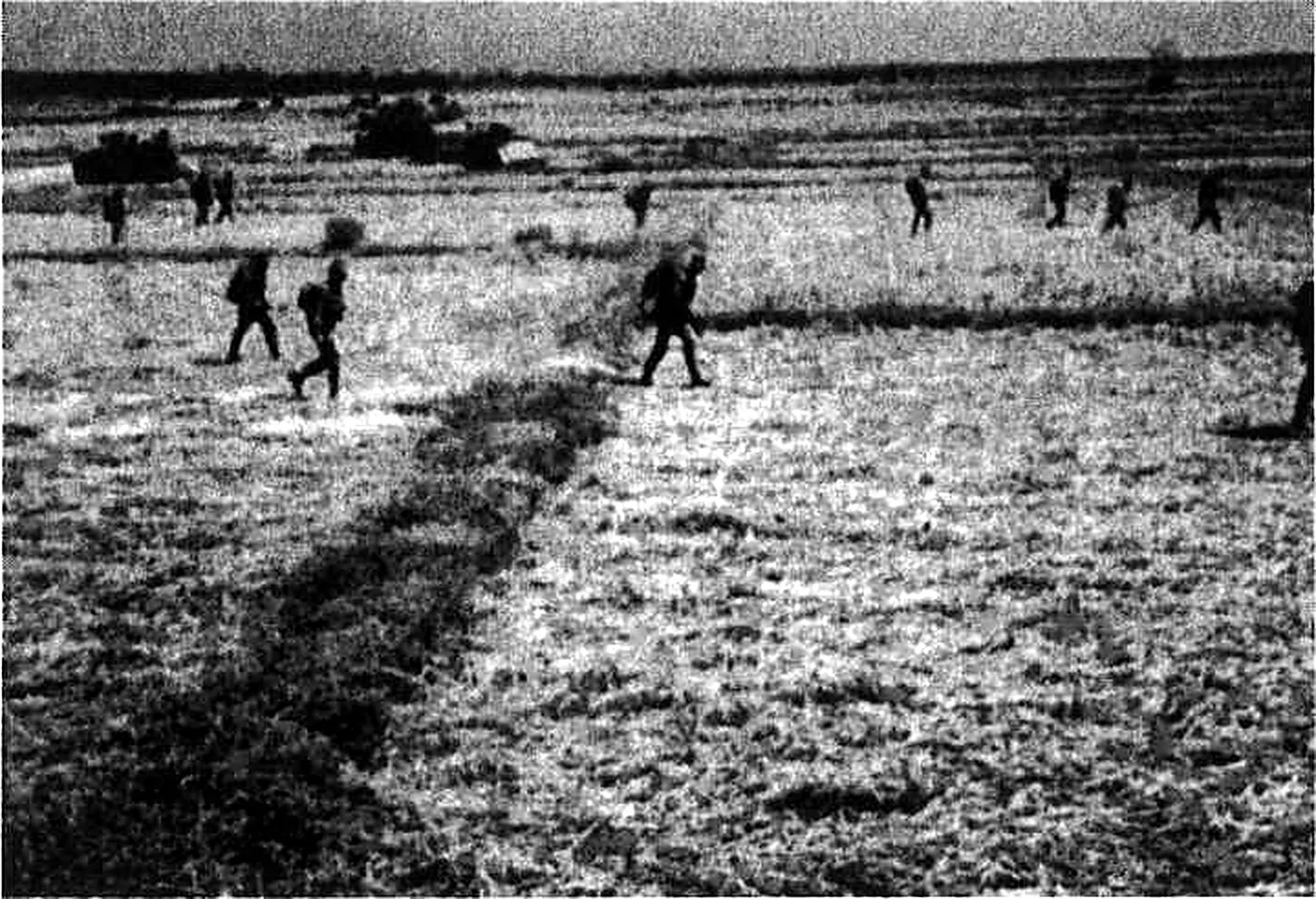 Soldiers advancing in extended line across flooded paddy fields with armoured vehicles behind
